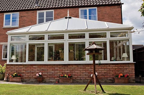 A white conservatory in front of a brick house.